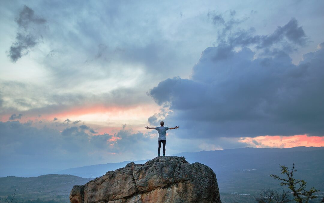 Christian with arms outstretched on top of mountain